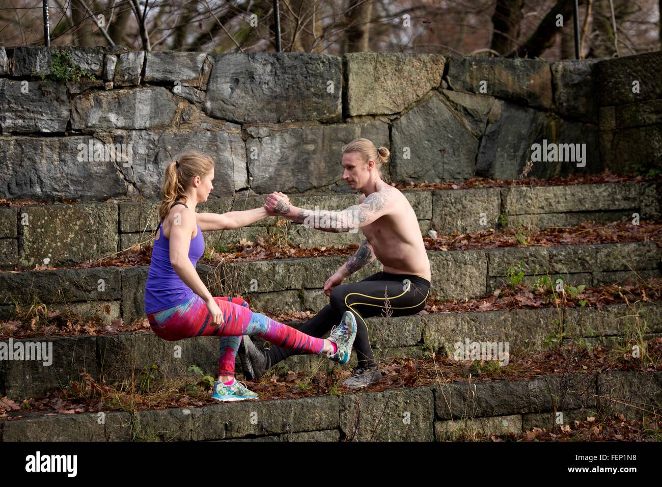 Side view of couple squatting on stone steps, face to face holding hands balancing on one leg Stock Photo