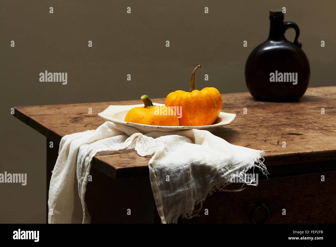 Pumpkins in serving dish on table with brown glass bottle Stock Photo