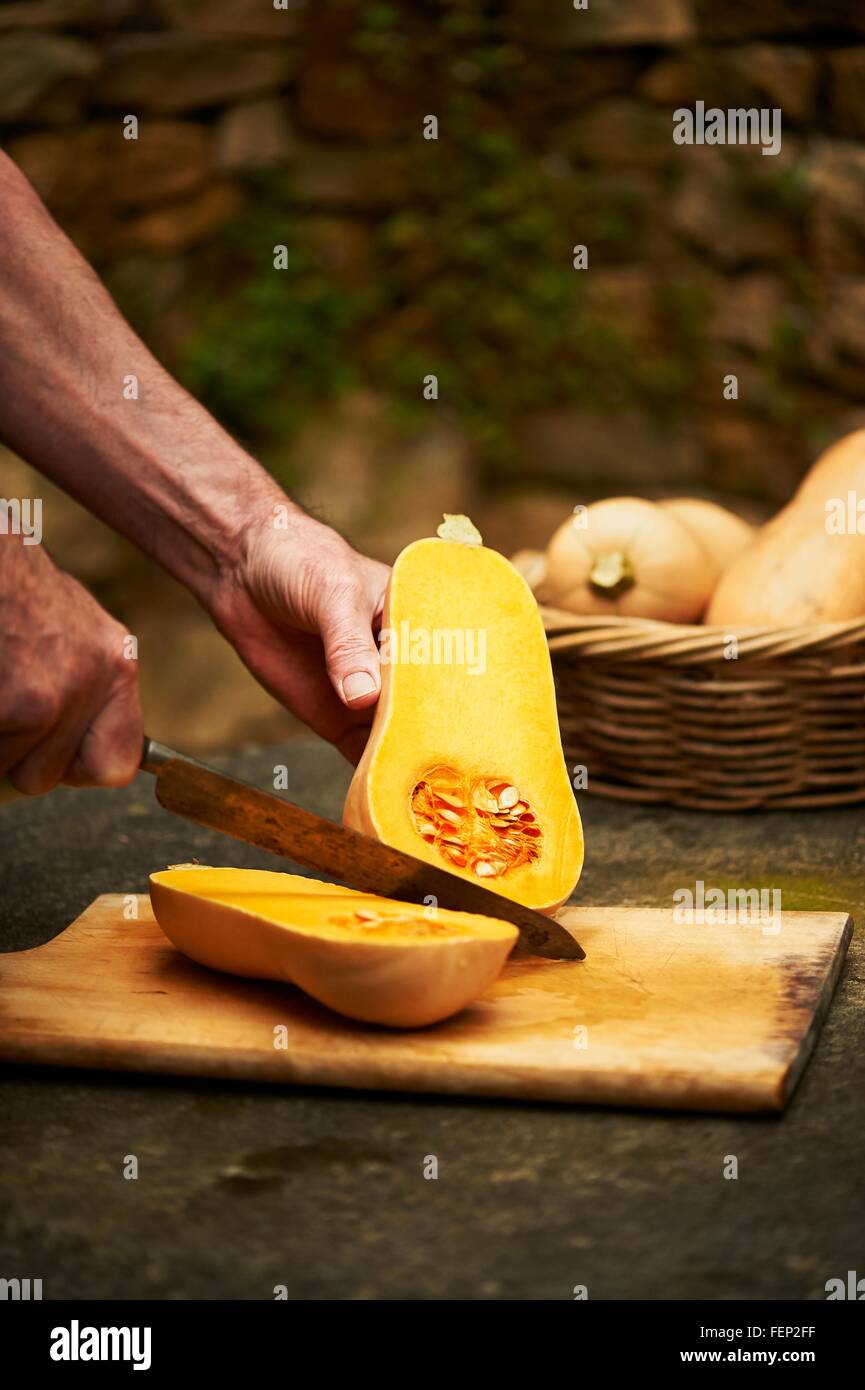 Senior mans hands chopping butternut squash with knife on cutting board