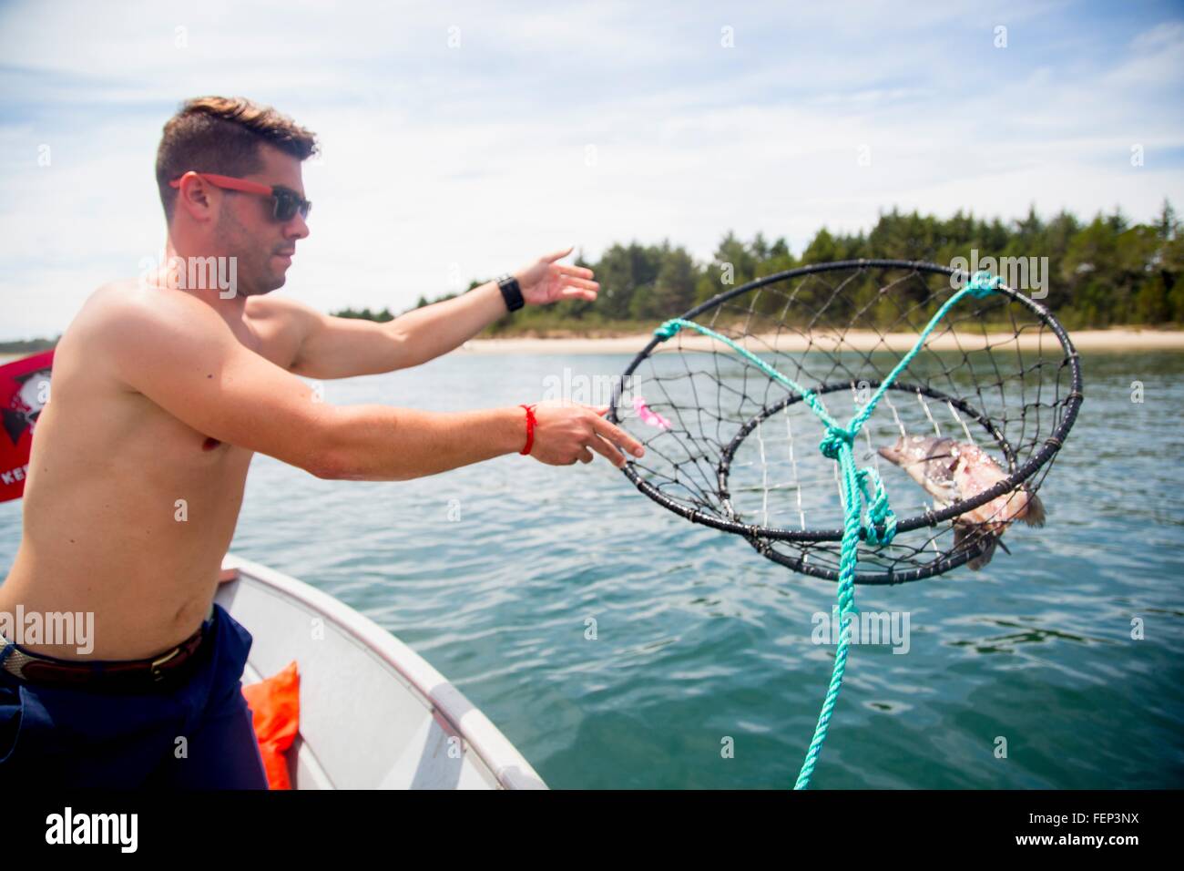 Mid adult man throwing baited crab trap from fishing boat, Nehalem Bay, Oregon, USA Stock Photo