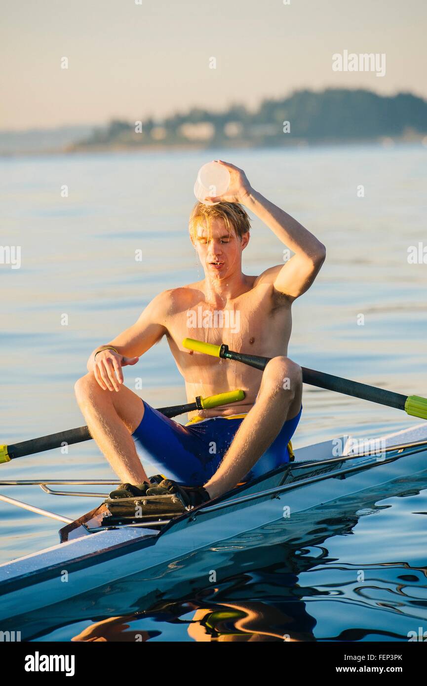 Teenage boy in sculling boat, pouring water over head to cool him down Stock Photo