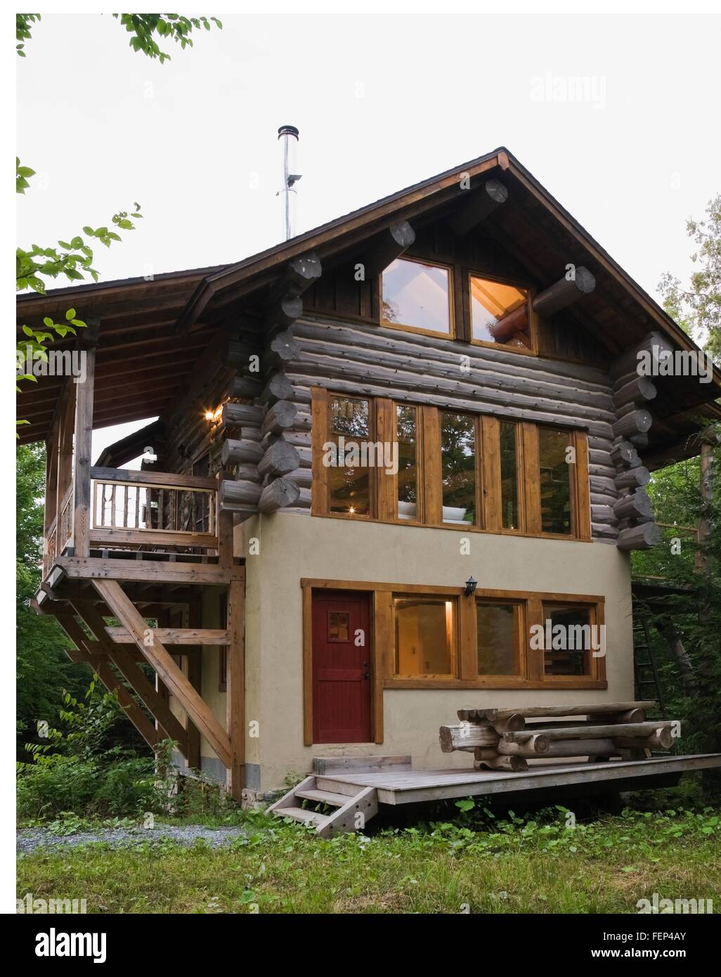 Cottage style log home facade with beige stucco finish and timber wood  balcony in summer Stock Photo - Alamy
