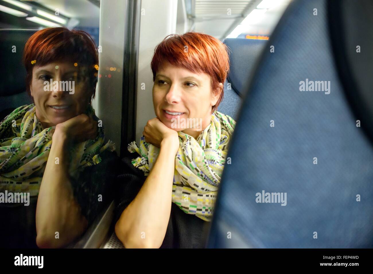 Mature woman looking through window whilst sitting on train at night Stock Photo