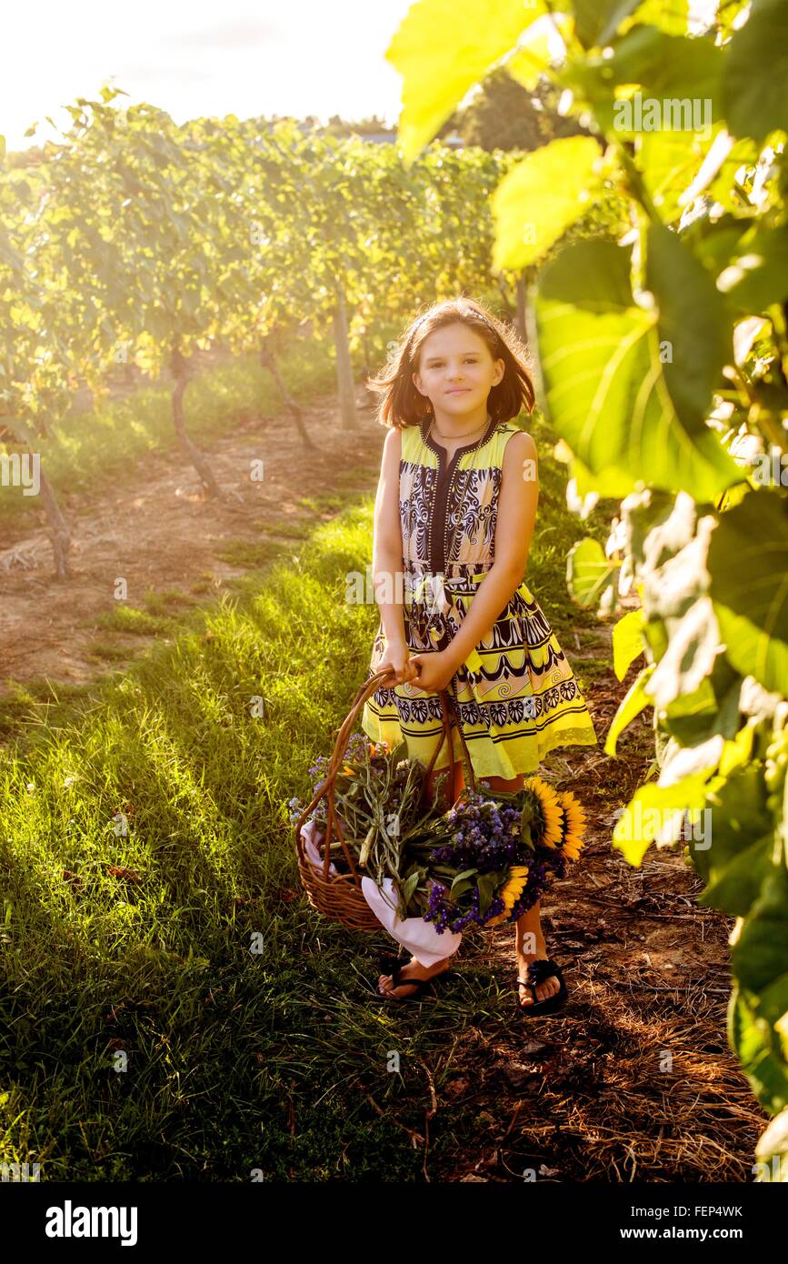 Portrait of girl carrying basket of flowers in vineyard Stock Photo