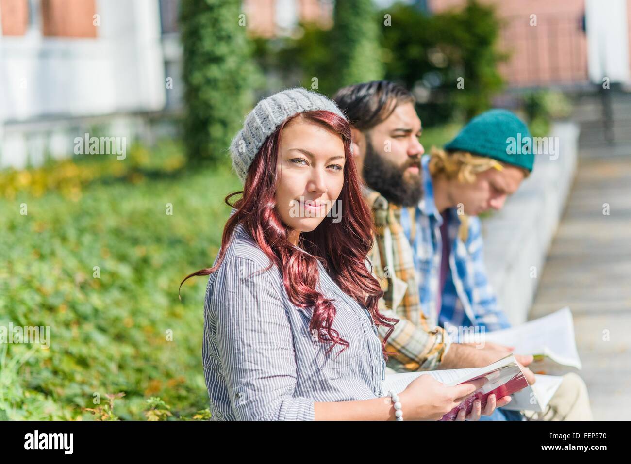 Portrait of adult college students reading books on campus wall Stock Photo