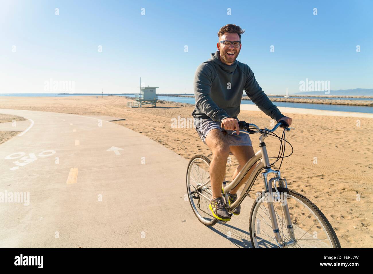 Young man cycling along pathway at beach Stock Photo