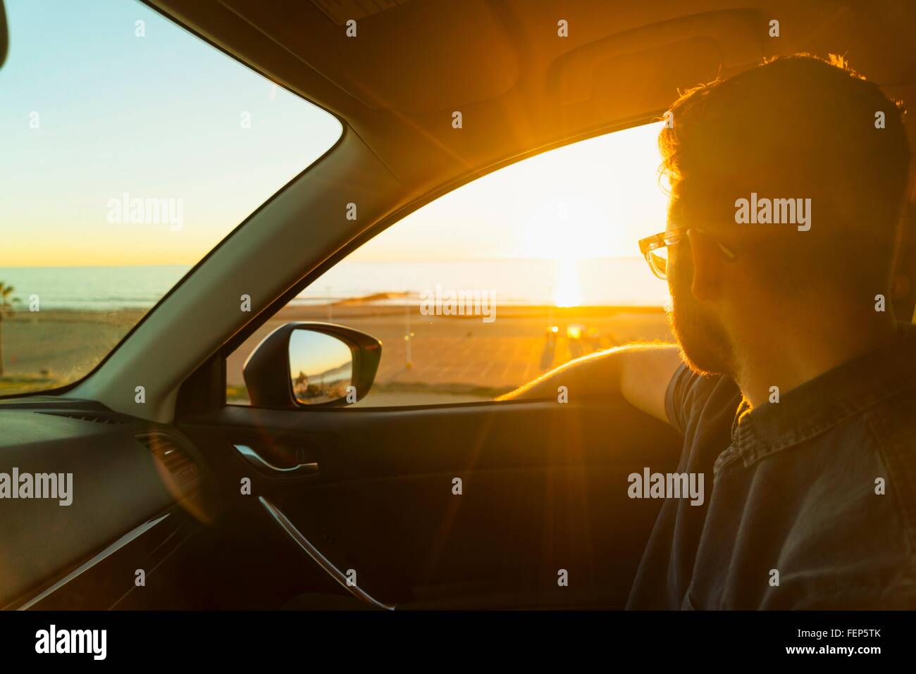 Young man looking out of car window at sunset Stock Photo