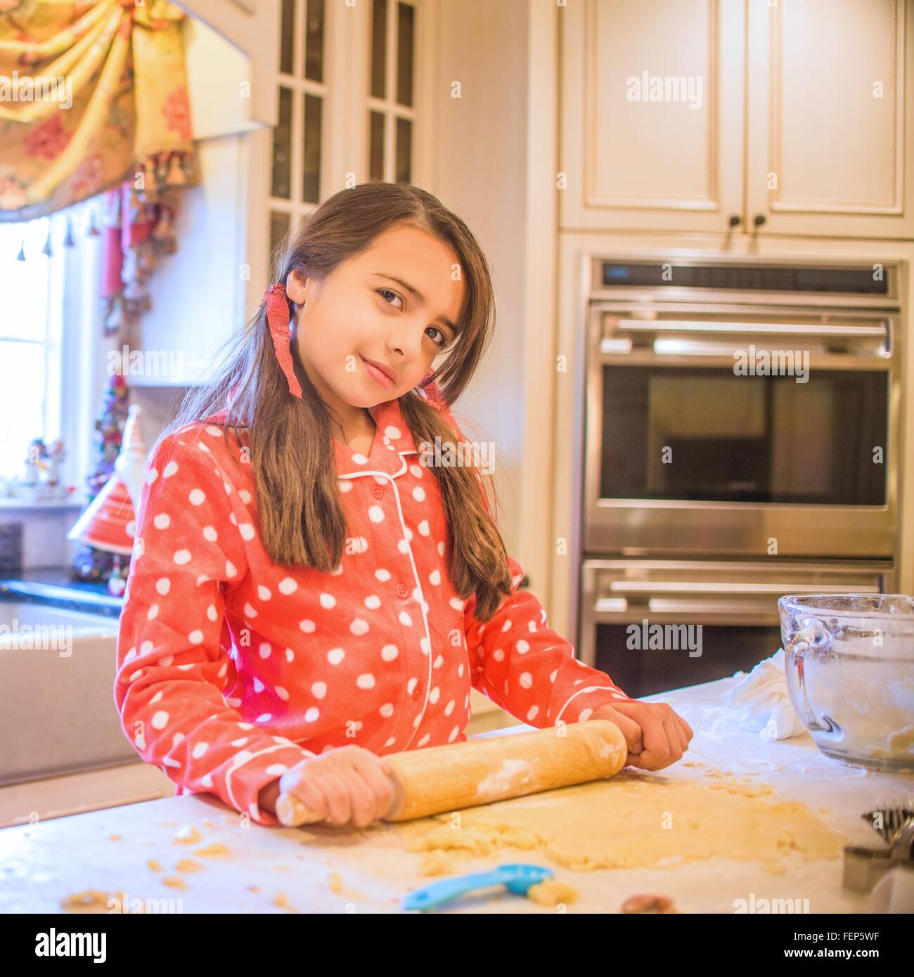 Portrait of young girl in kitchen, using rolling pin Stock Photo