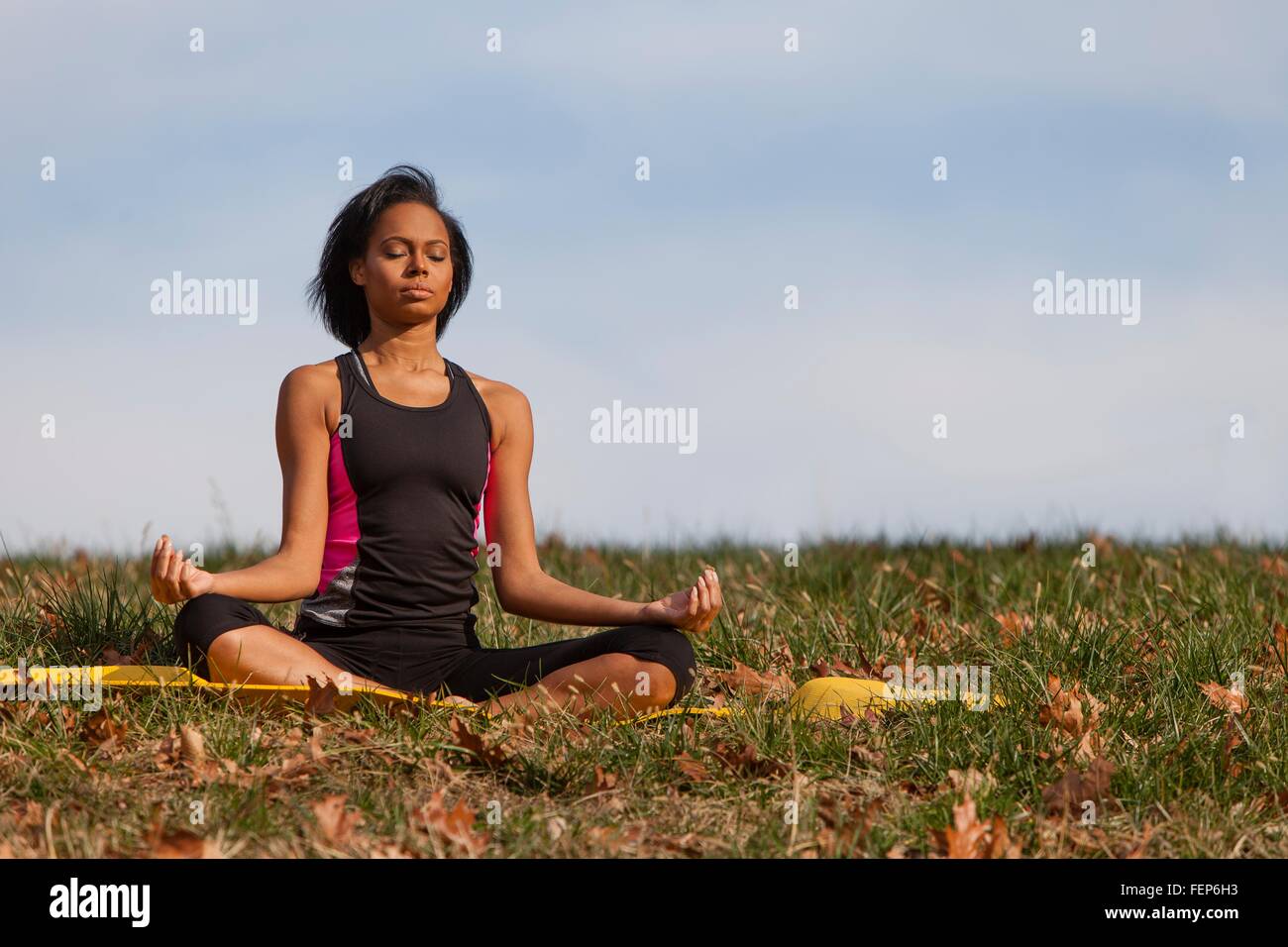 Young woman sitting on yoga mat, outdoors, in lotus position Stock ...