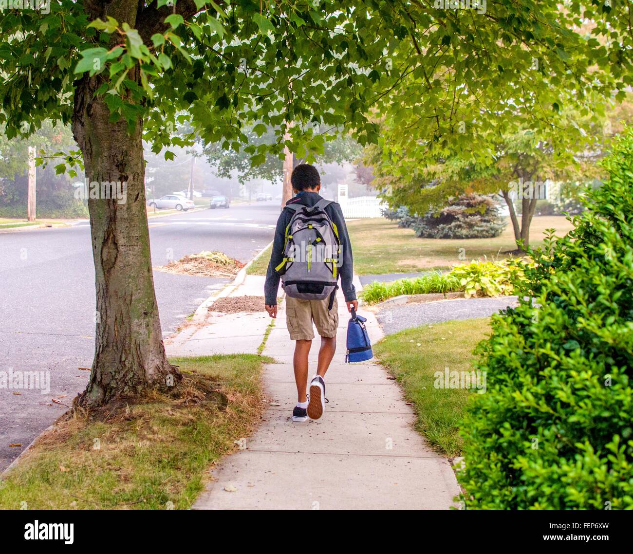 Boy with backpack walking on sidewalk Stock Photo