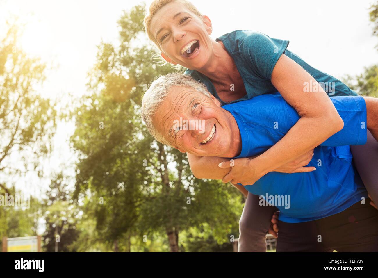 Senior man carrying mature woman on back, outdoors, laughing Stock Photo