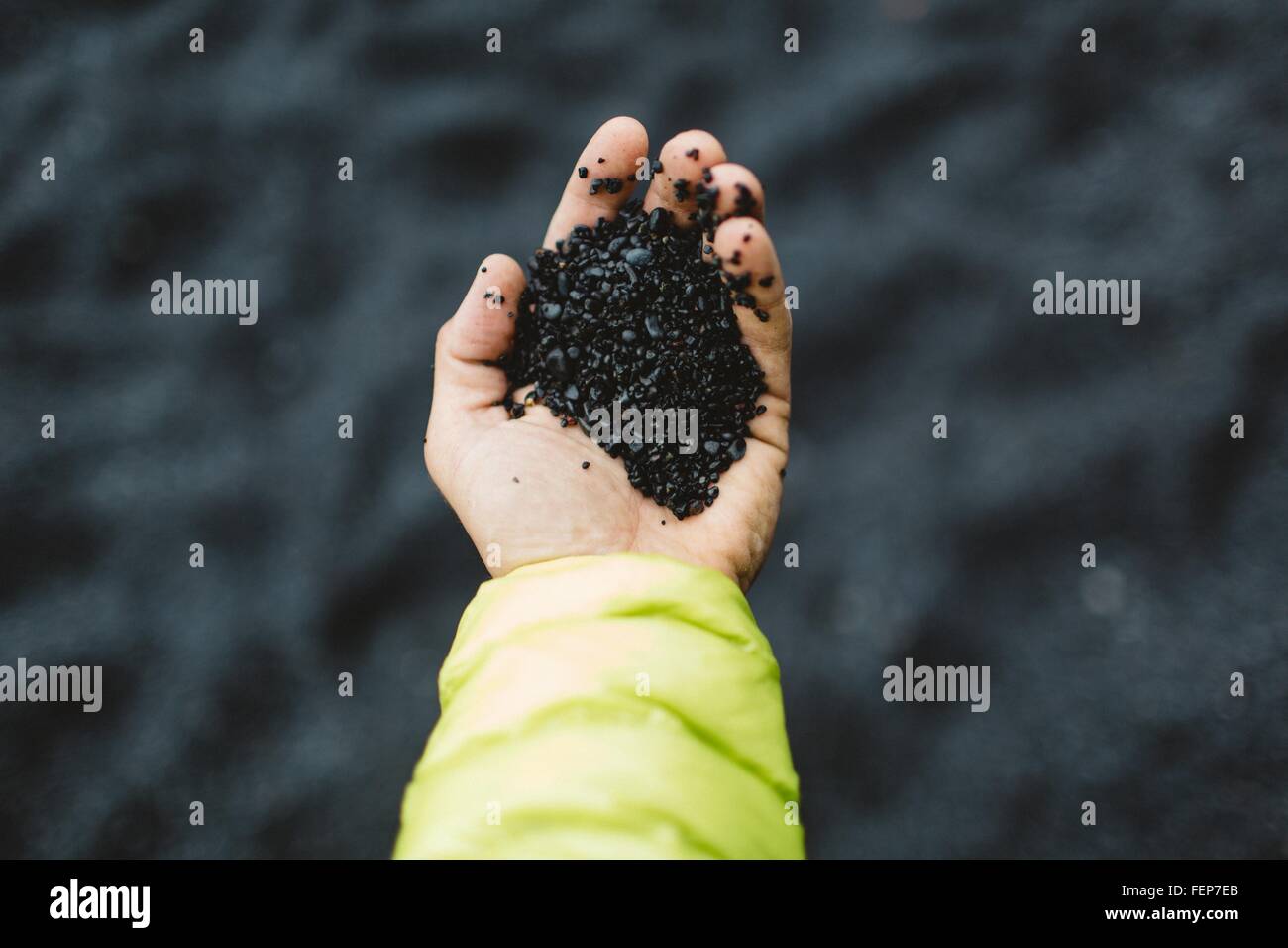 Hand of mid adult man holding black sand, overhead view, Iceland Stock Photo