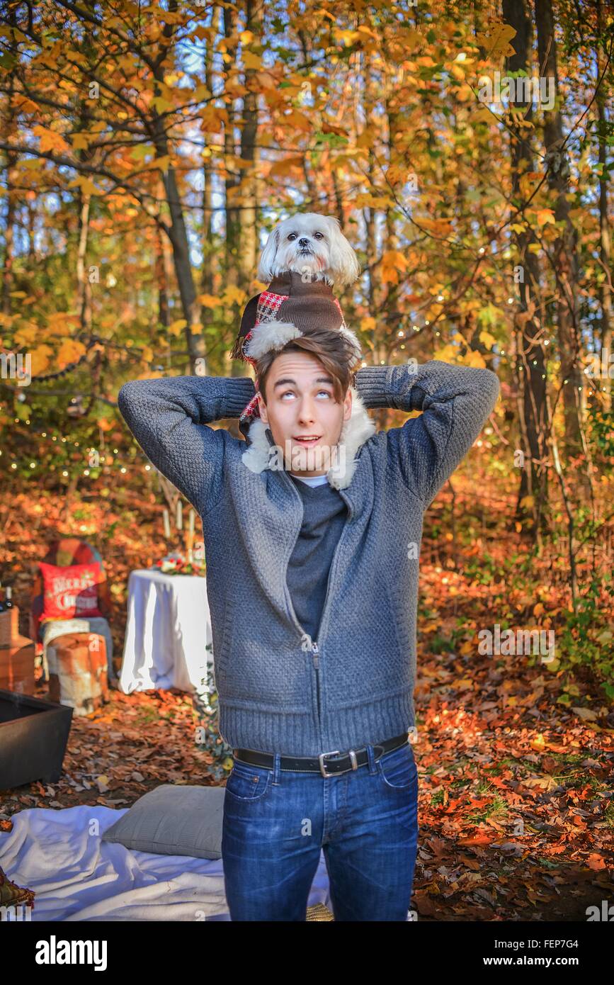 Portrait of young man carrying dog on shoulders in woods Stock Photo
