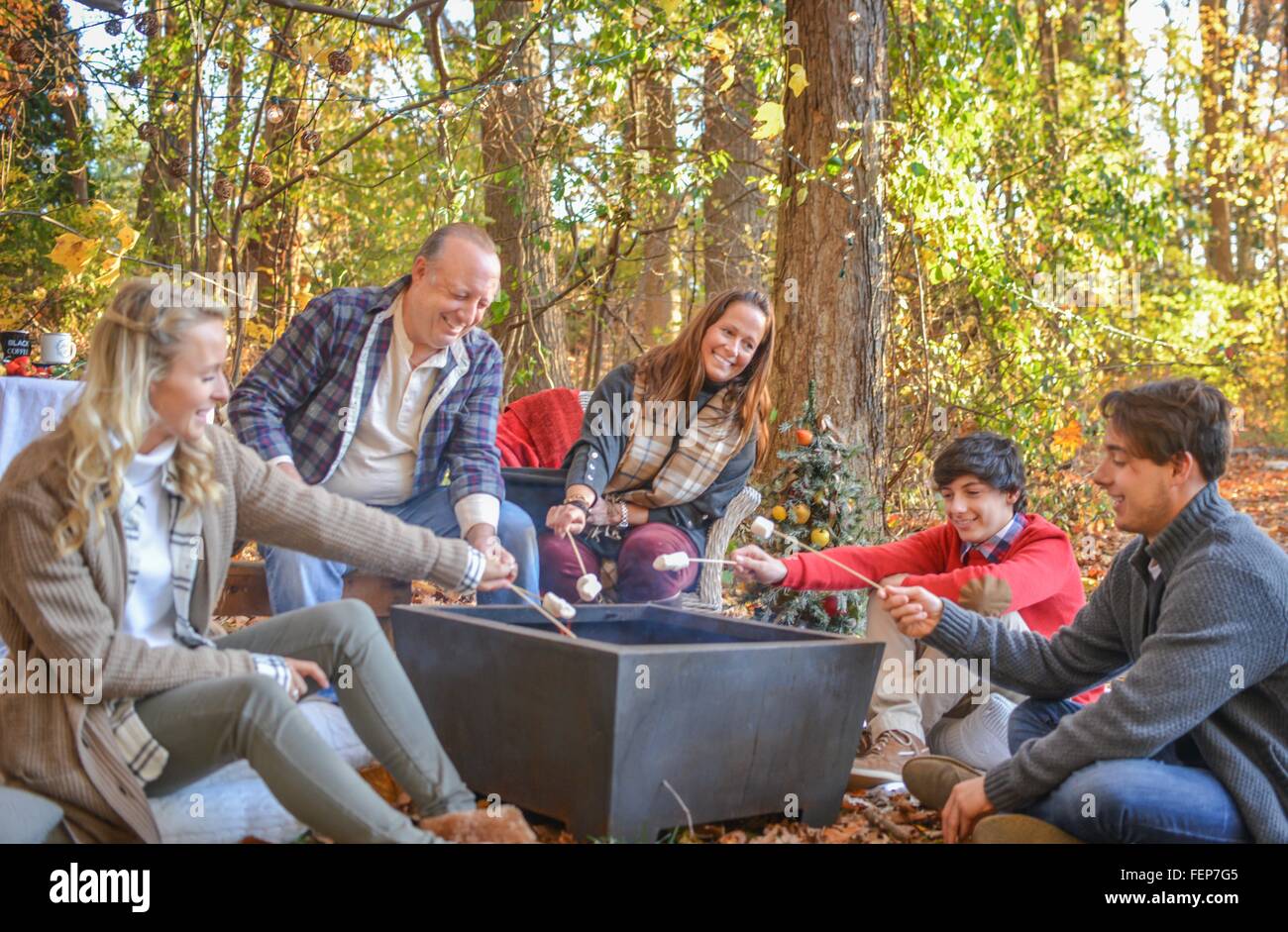 Parents with adult and teenage children toasting marshmallows in woods Stock Photo