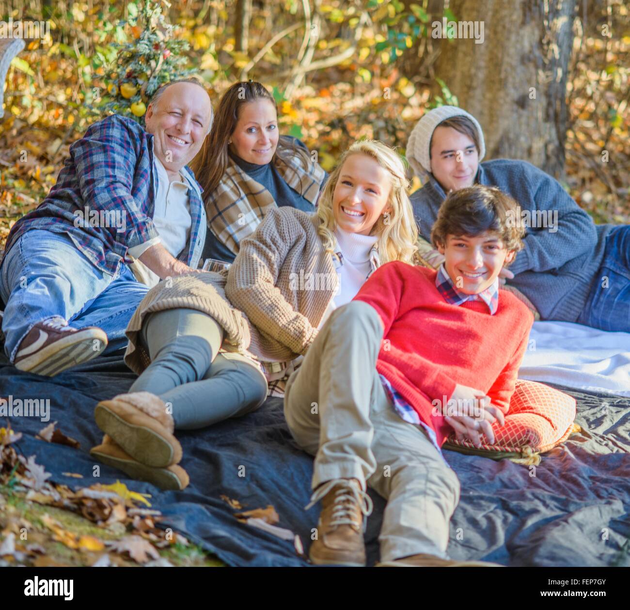 Portrait of mature couple with teenage and adult children relaxing on picnic blanket in woods Stock Photo