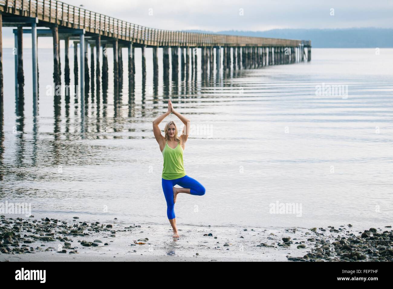 Portrait of young woman practicing yoga standing tree pose on beach ...