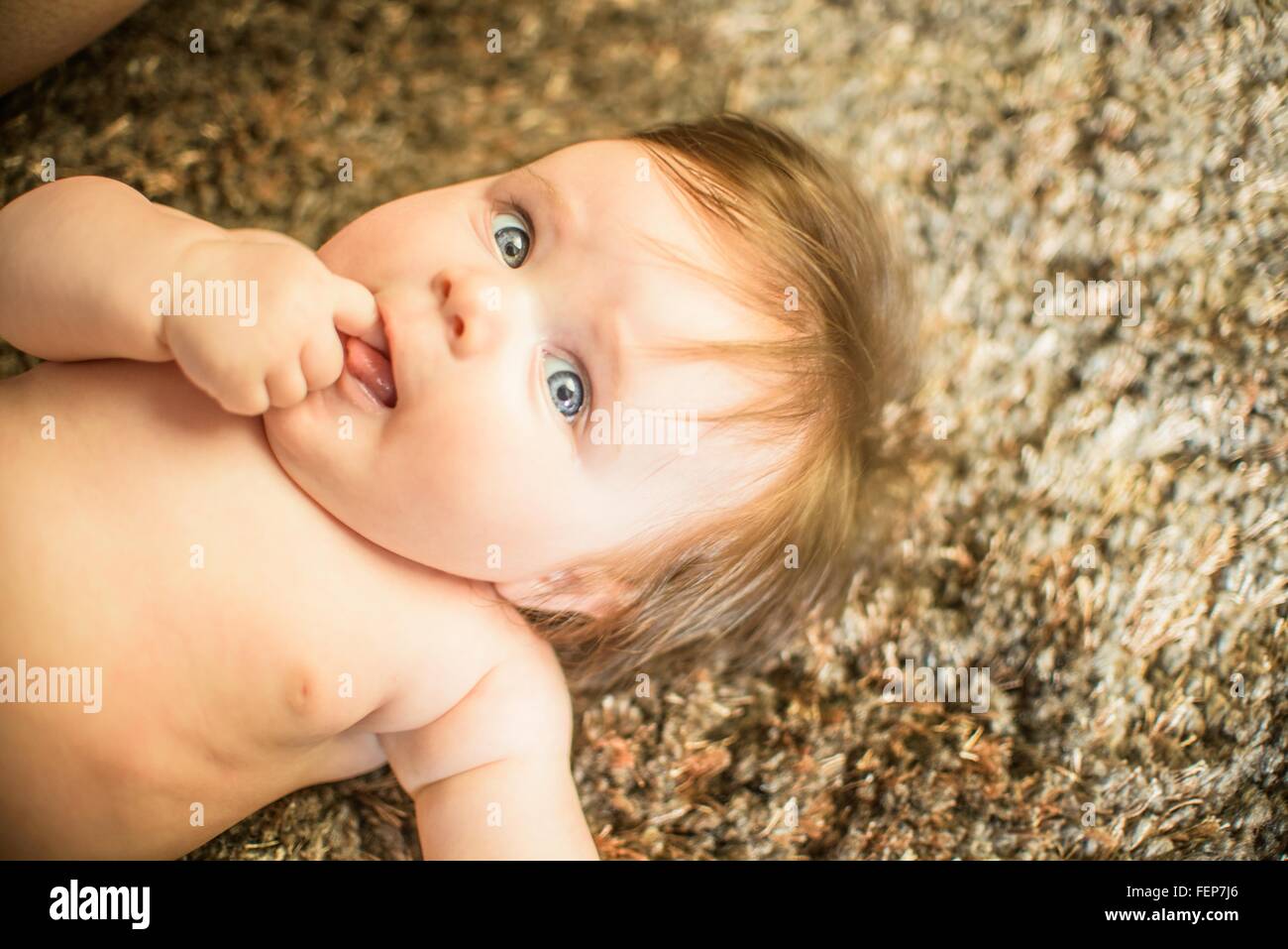 High angle view of baby girl lying on carpet, finger in mouth looking away Stock Photo