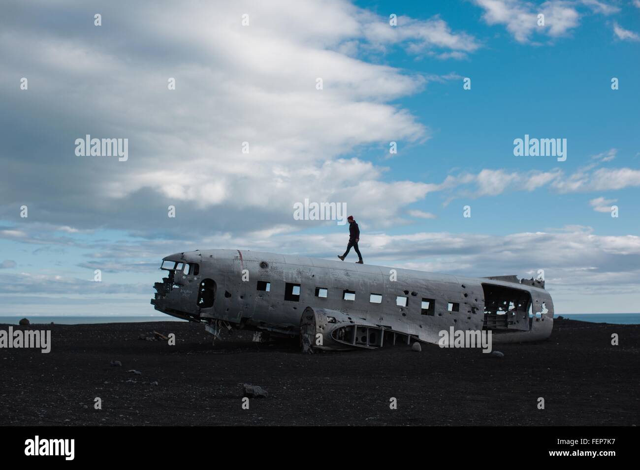 Side view of mid adult man walking on top of airplane wreckage on volcanic landscape, Iceland Stock Photo