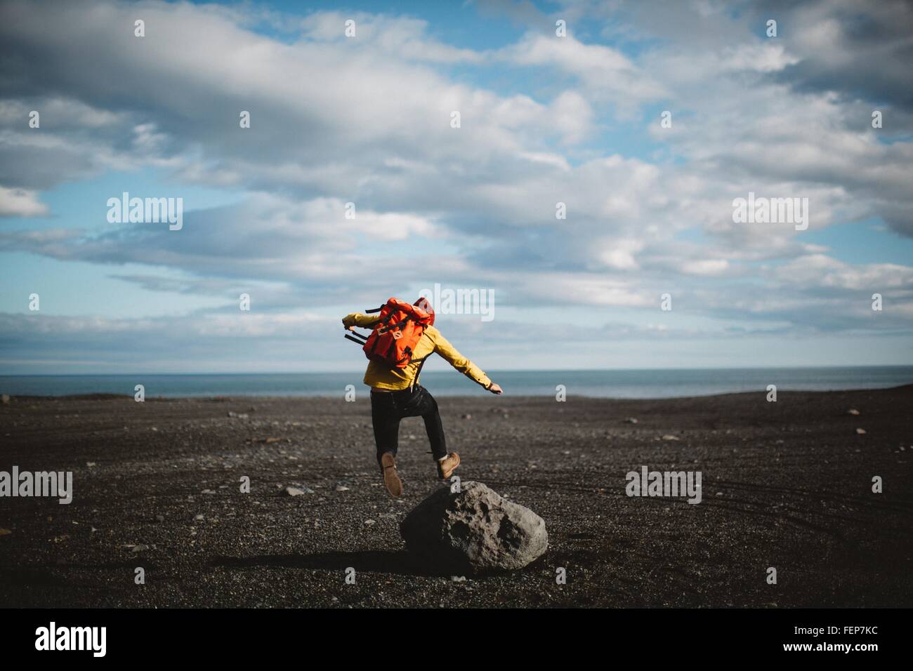 Rear view of mid adult man jumping over boulder on volcanic landscape, Iceland Stock Photo