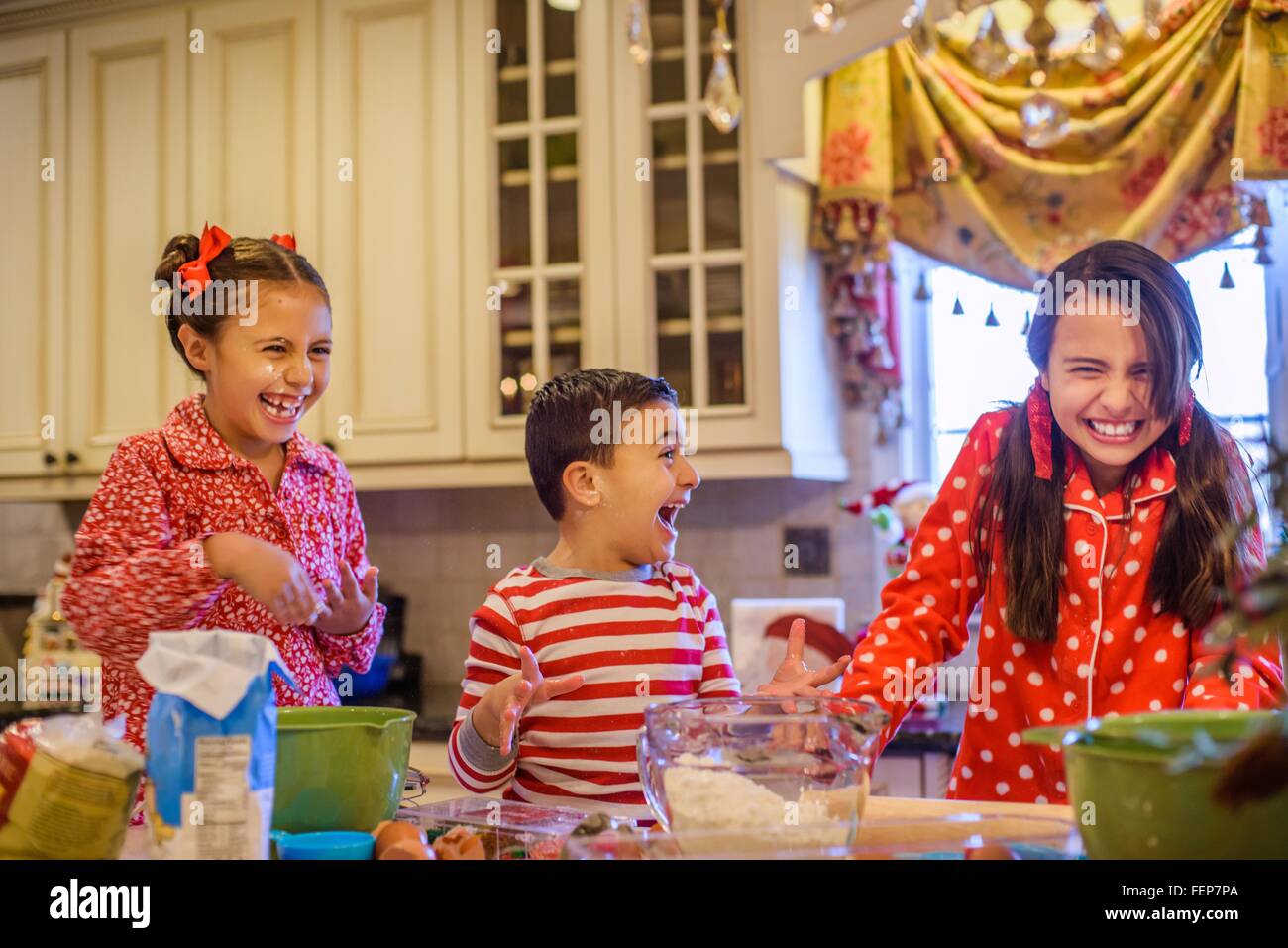 Children wearing pyjamas at kitchen counter baking, laughing Stock Photo