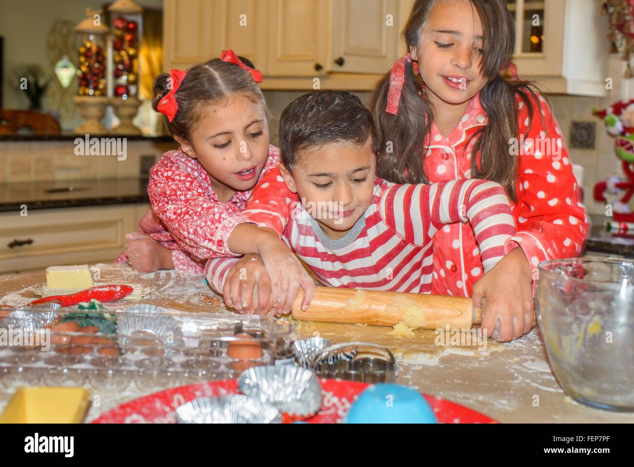 Children in kitchen wearing pyjamas rolling out dough with rolling pin Stock Photo