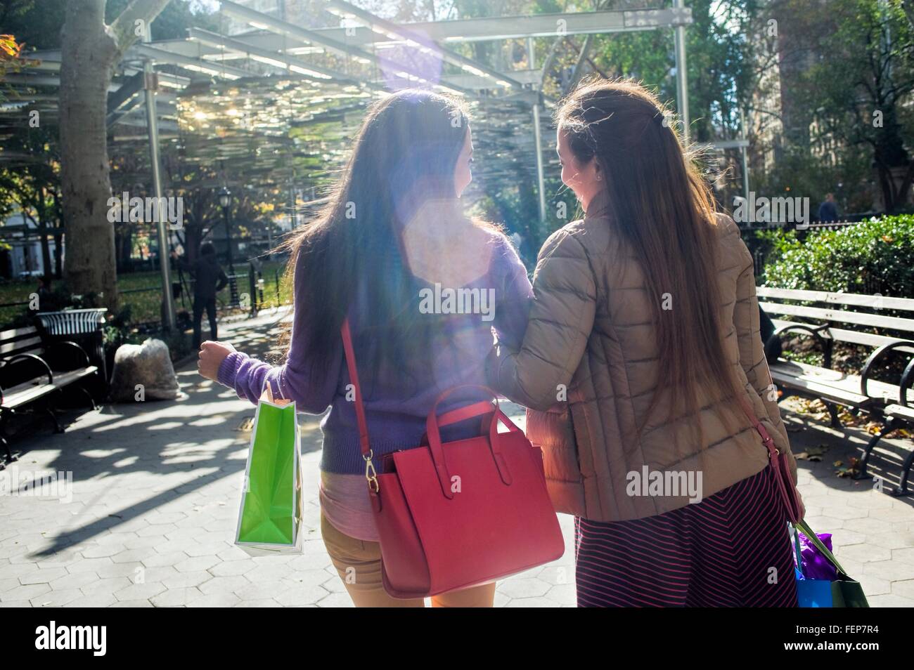 Rear view of young female adult twins strolling in park with shopping bags Stock Photo