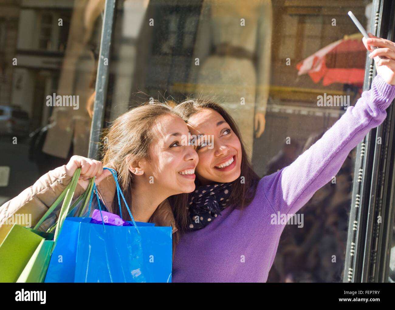 Young female adult twins in city taking selfie on smartphone with shopping bags Stock Photo