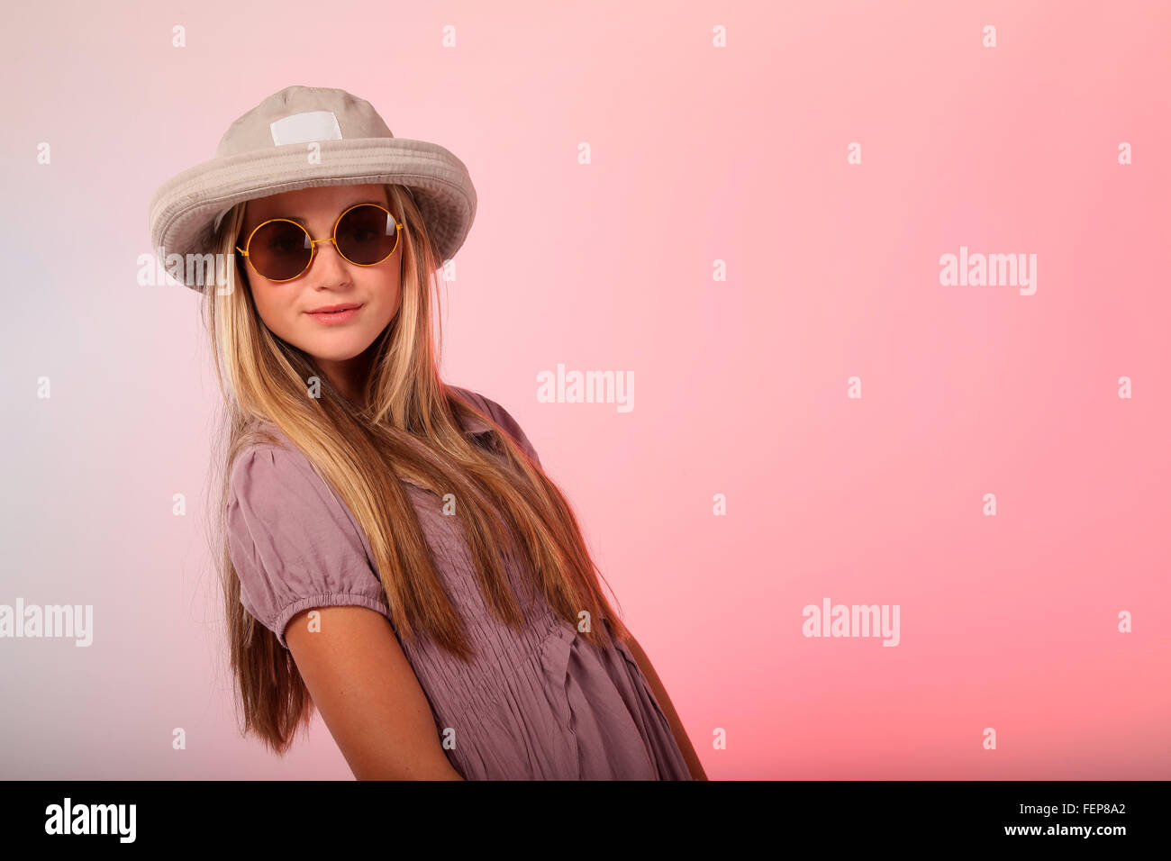 A beautiful blond teenage girl wearing sunglasses in studio, she also has a hat on her head. Stock Photo