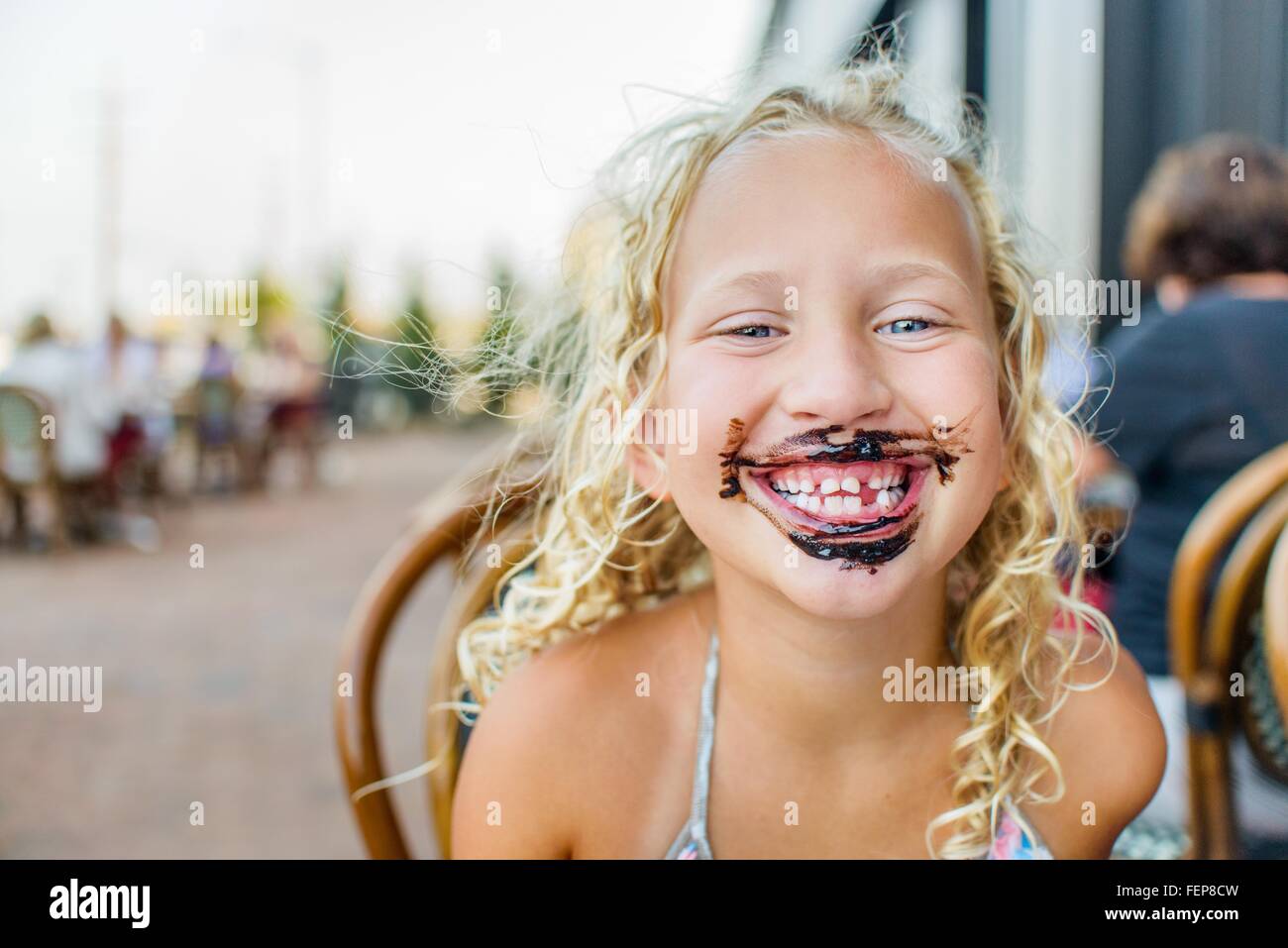 Portrait of blond haired girl at sidewalk cafe with sauce covered mouth Stock Photo