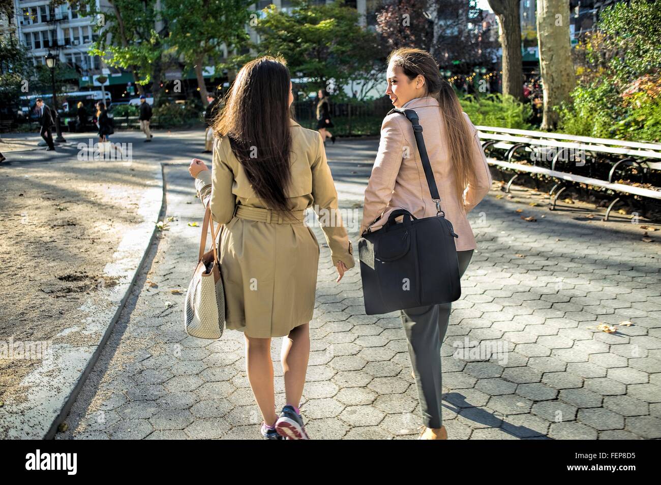 Rear view of young female twins walking through city park Stock Photo