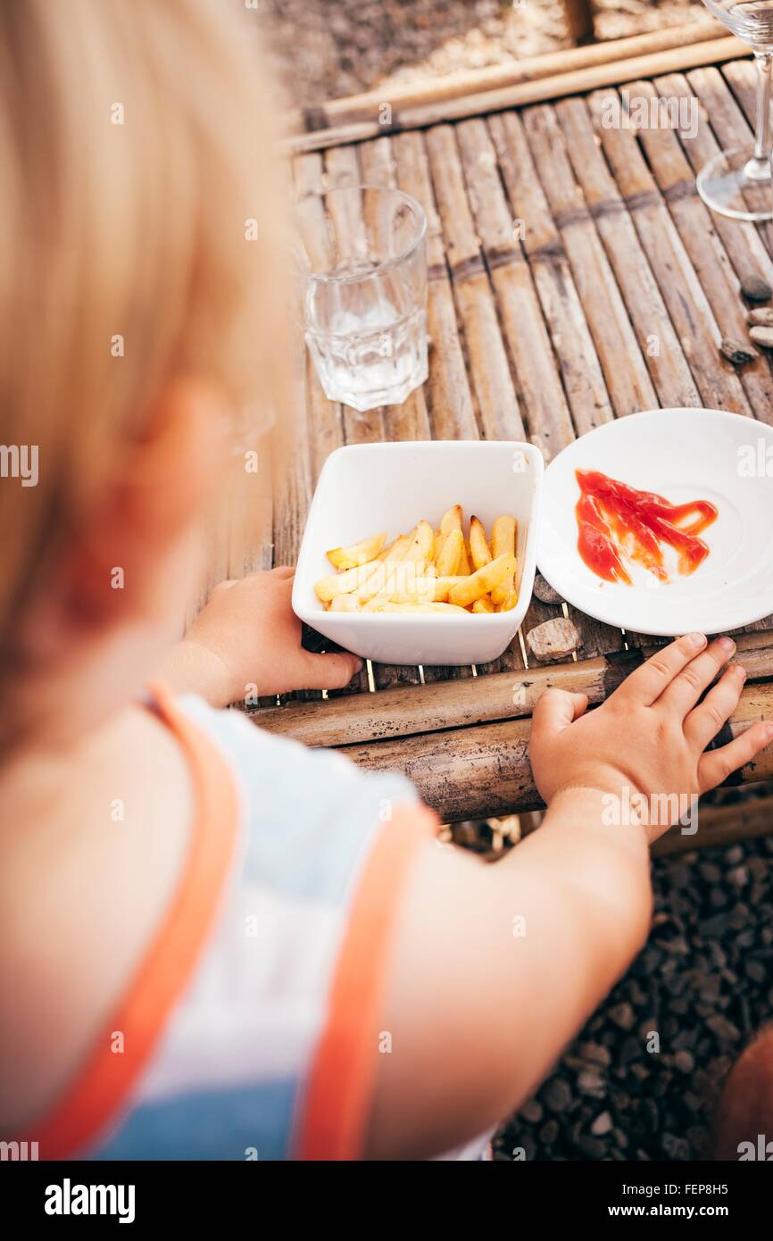 Over the shoulder view of boy eating french fries and ketchup Stock Photo