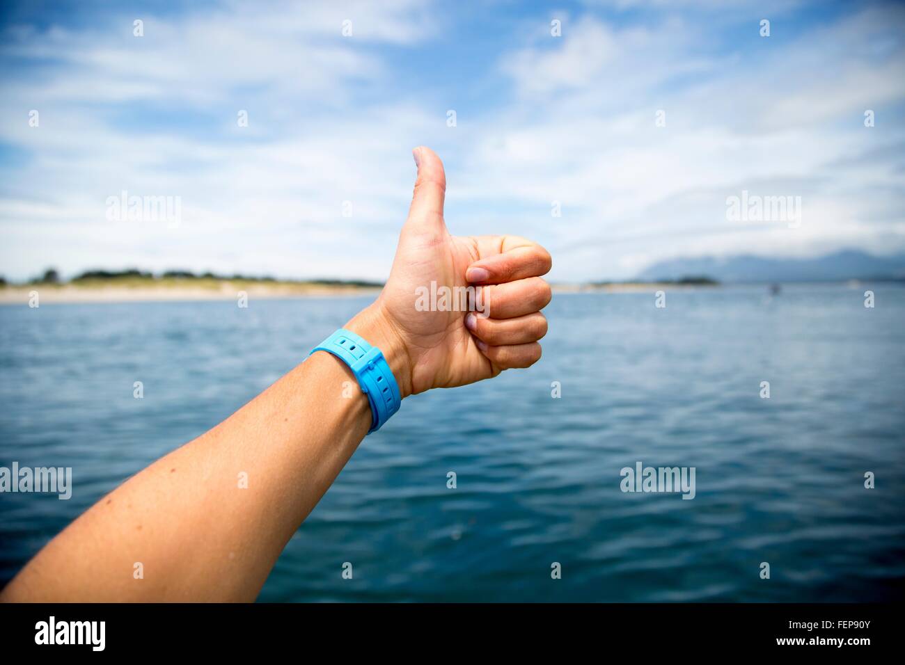 Female hand giving thumbs up over Nehalem Bay, Oregon, USA Stock Photo