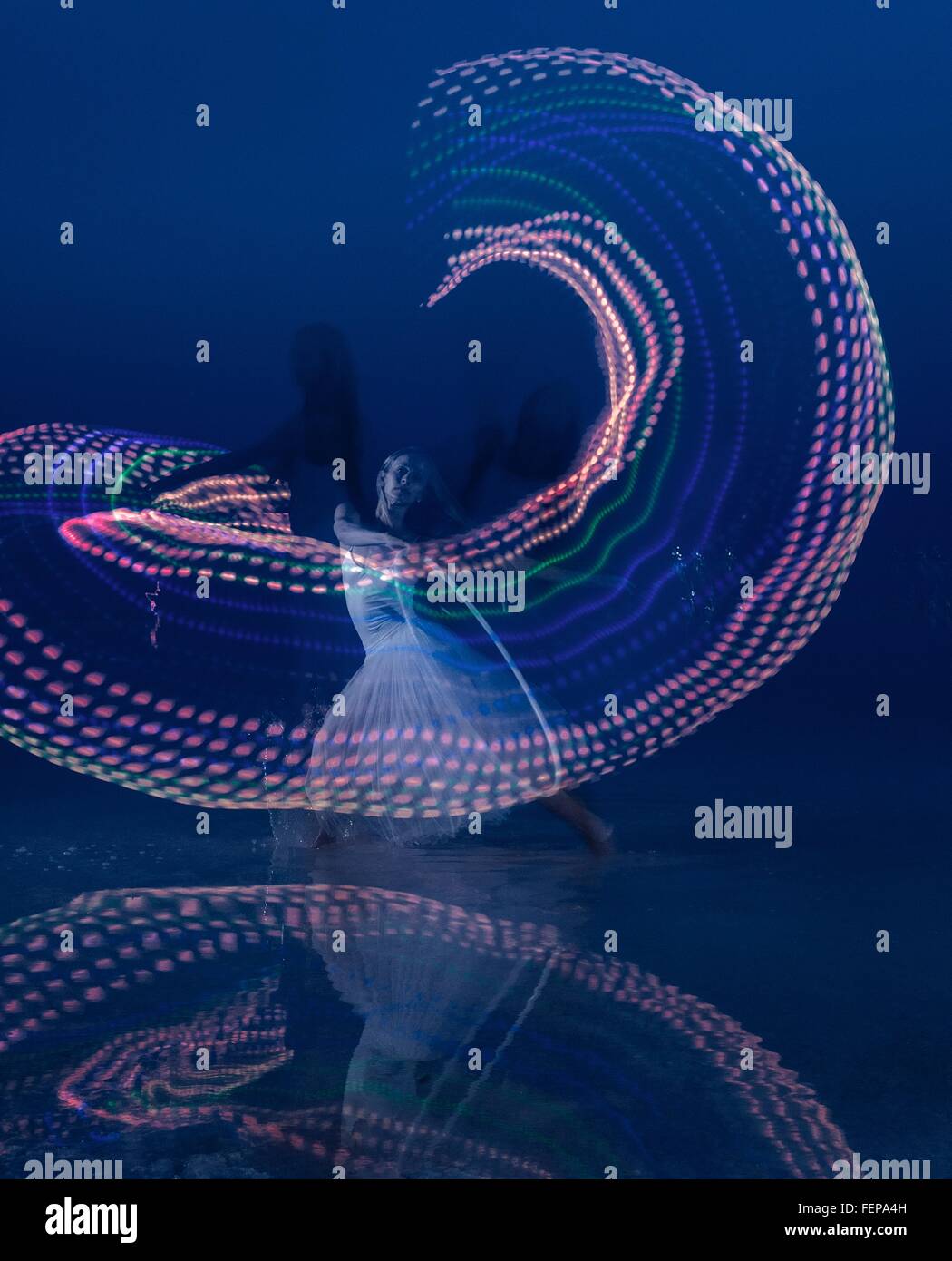 Woman dancing with illuminated multi-coloured hoop at dusk Stock Photo