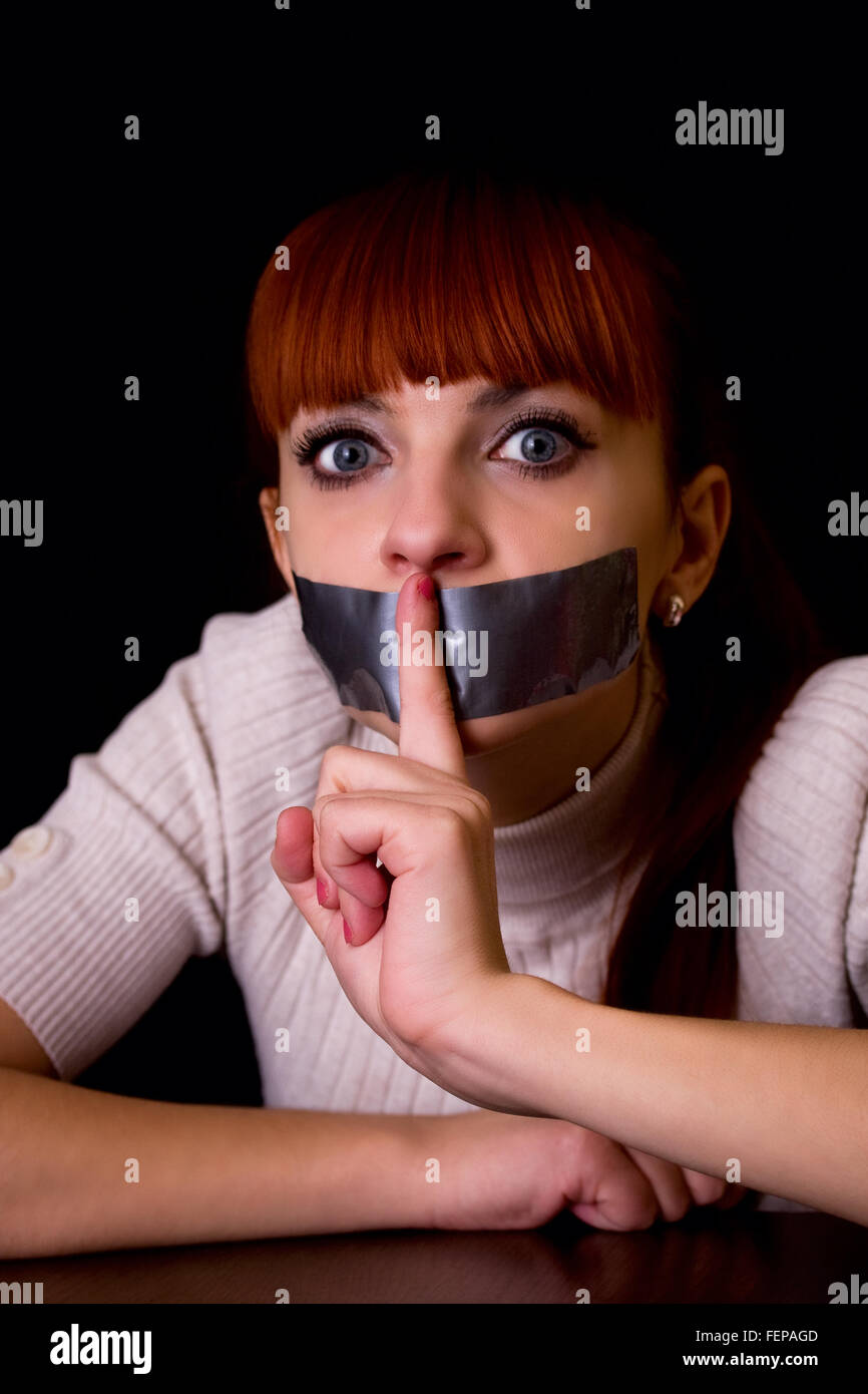 girl with her mouth sealed with tape brought finger to his mouth calling silent Stock Photo