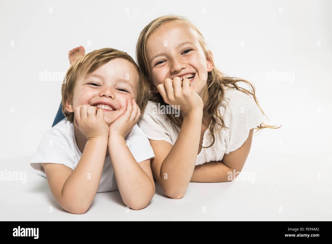 Studio portrait of happy boy and sister lying on their front Stock Photo