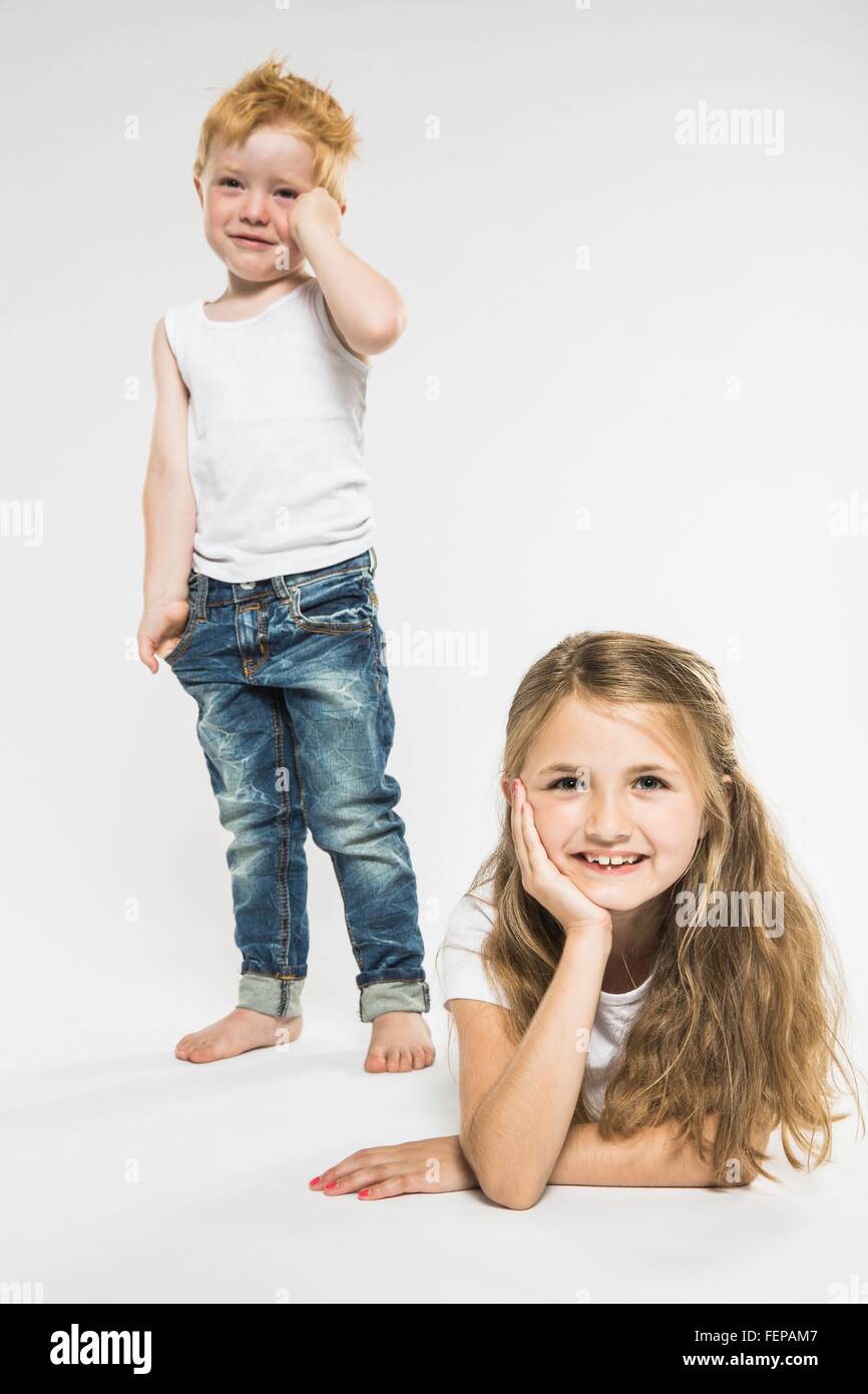 Studio portrait of happy girl lying on front whilst her brother is crying Stock Photo