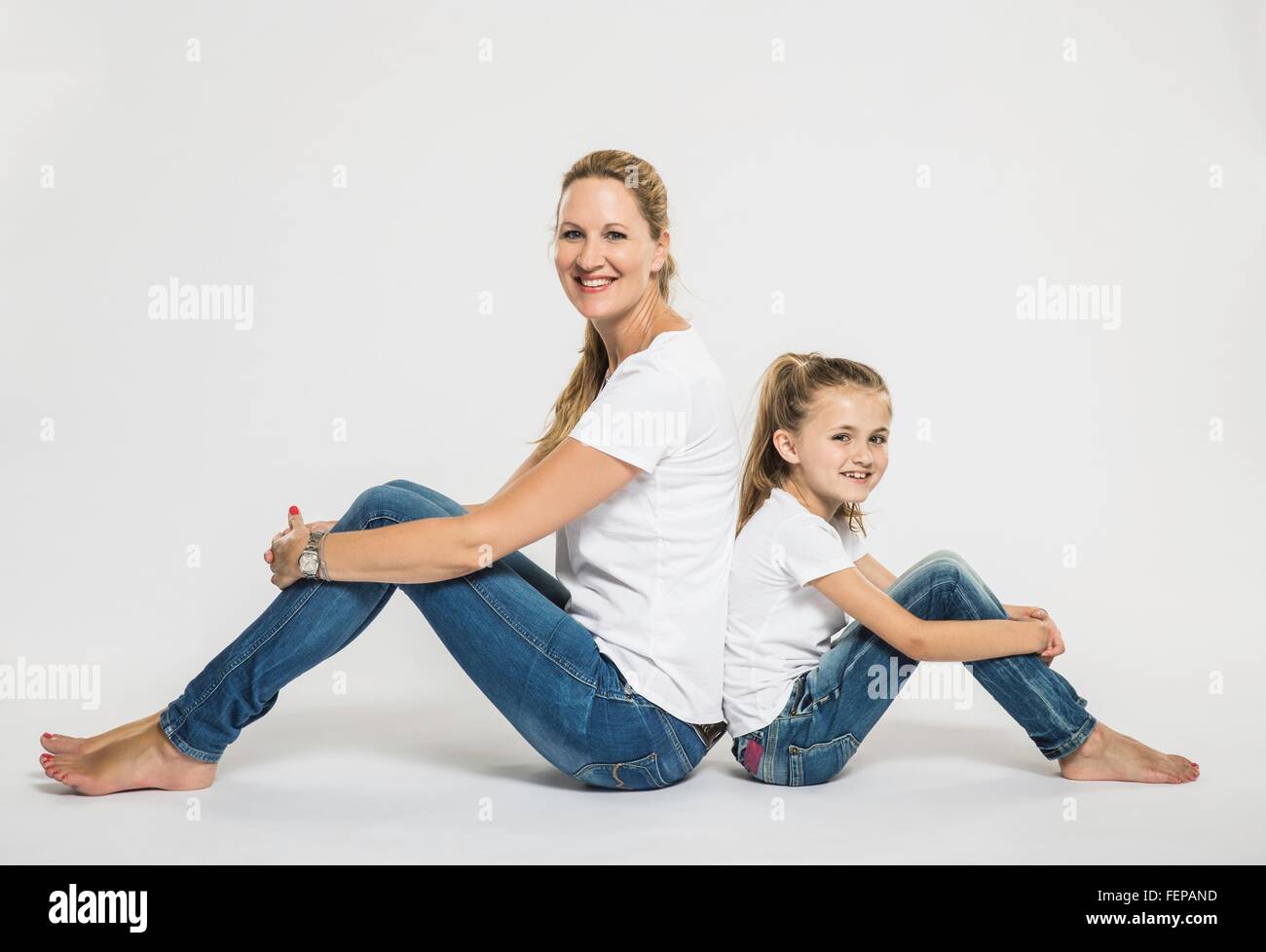 Studio portrait of girl and mother sitting back to back on floor Stock Photo