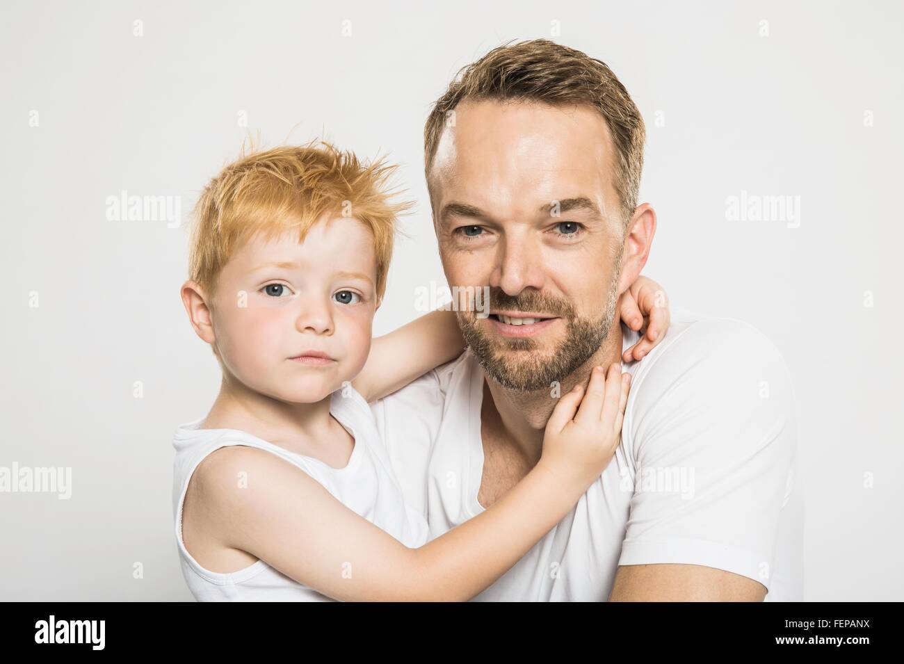 Studio portrait of boy with arms around his father Stock Photo