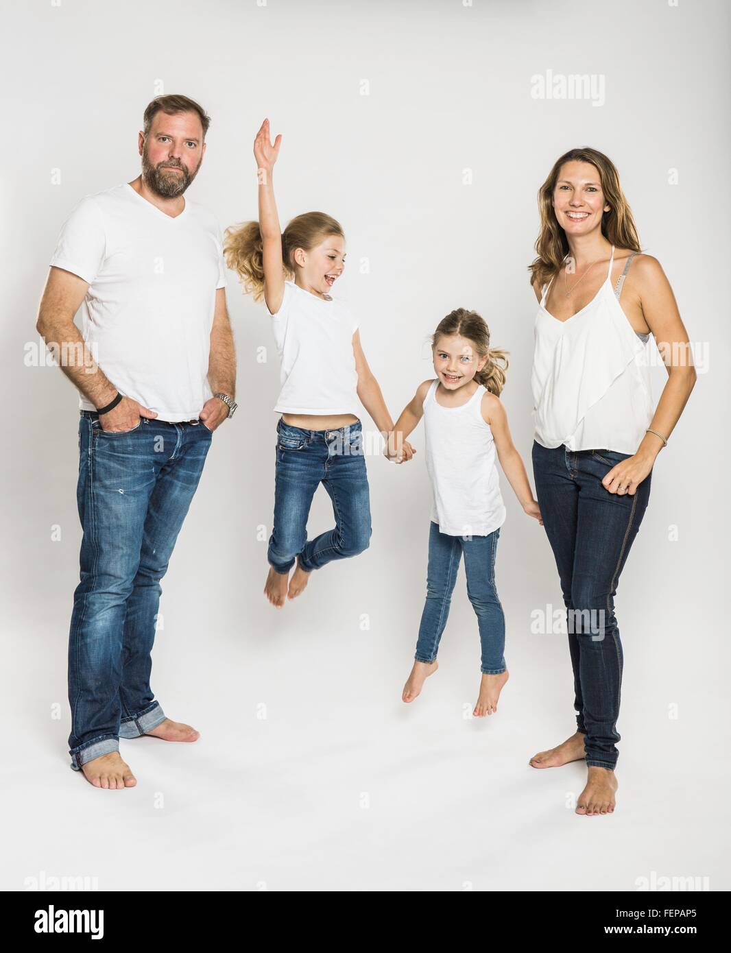 Studio portrait of two sisters jumping mid air between parents Stock Photo