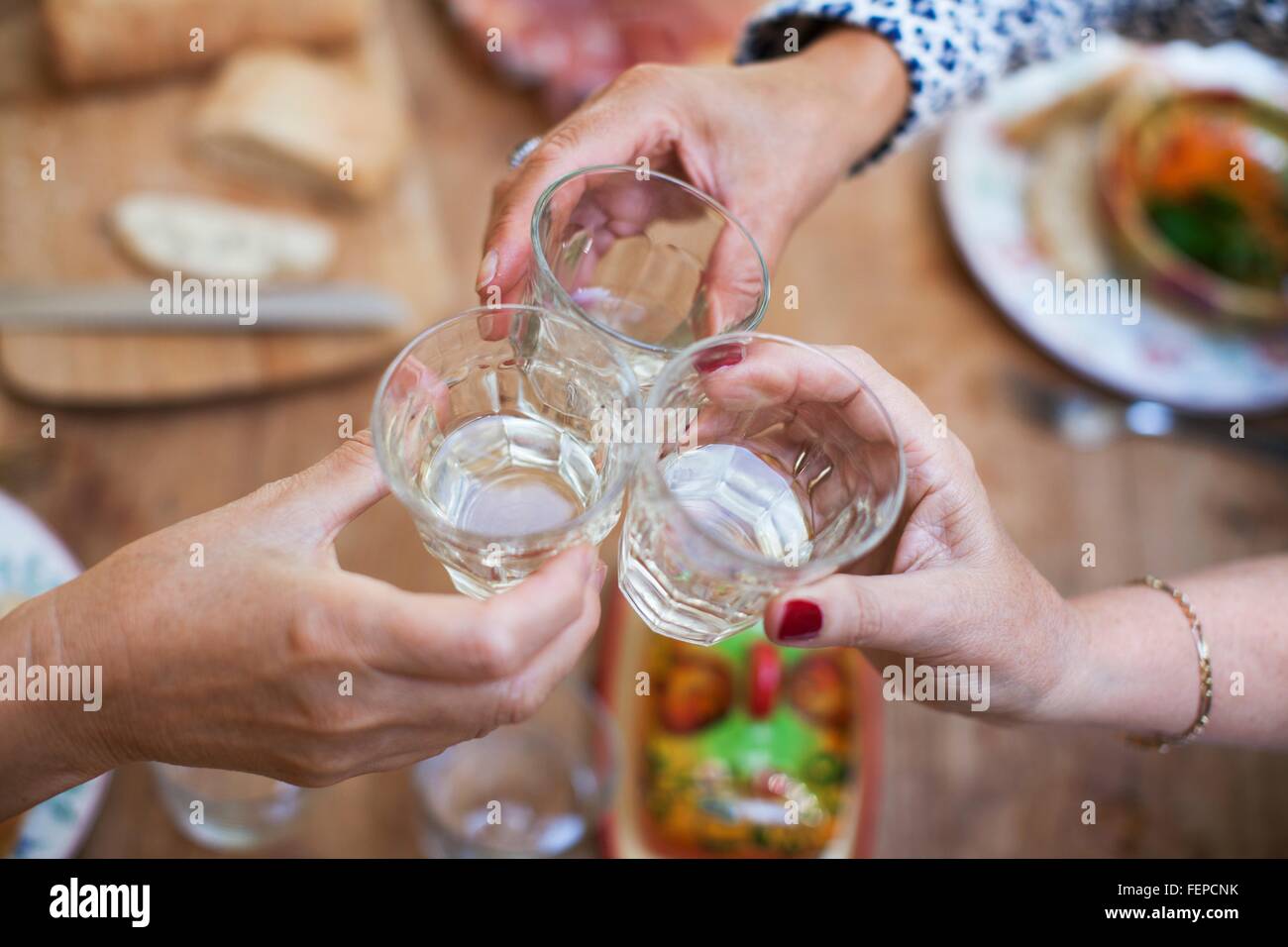 Three women having lunch together at home, making a toast, close-up of glasses Stock Photo