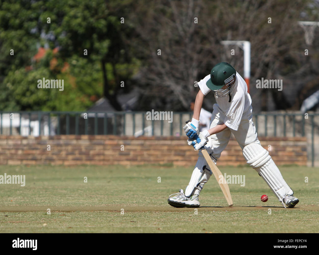 A schoolboy tries to block a cricket ball and prevent it from hitting his wickets. He is defensive mode but misses. Stock Photo