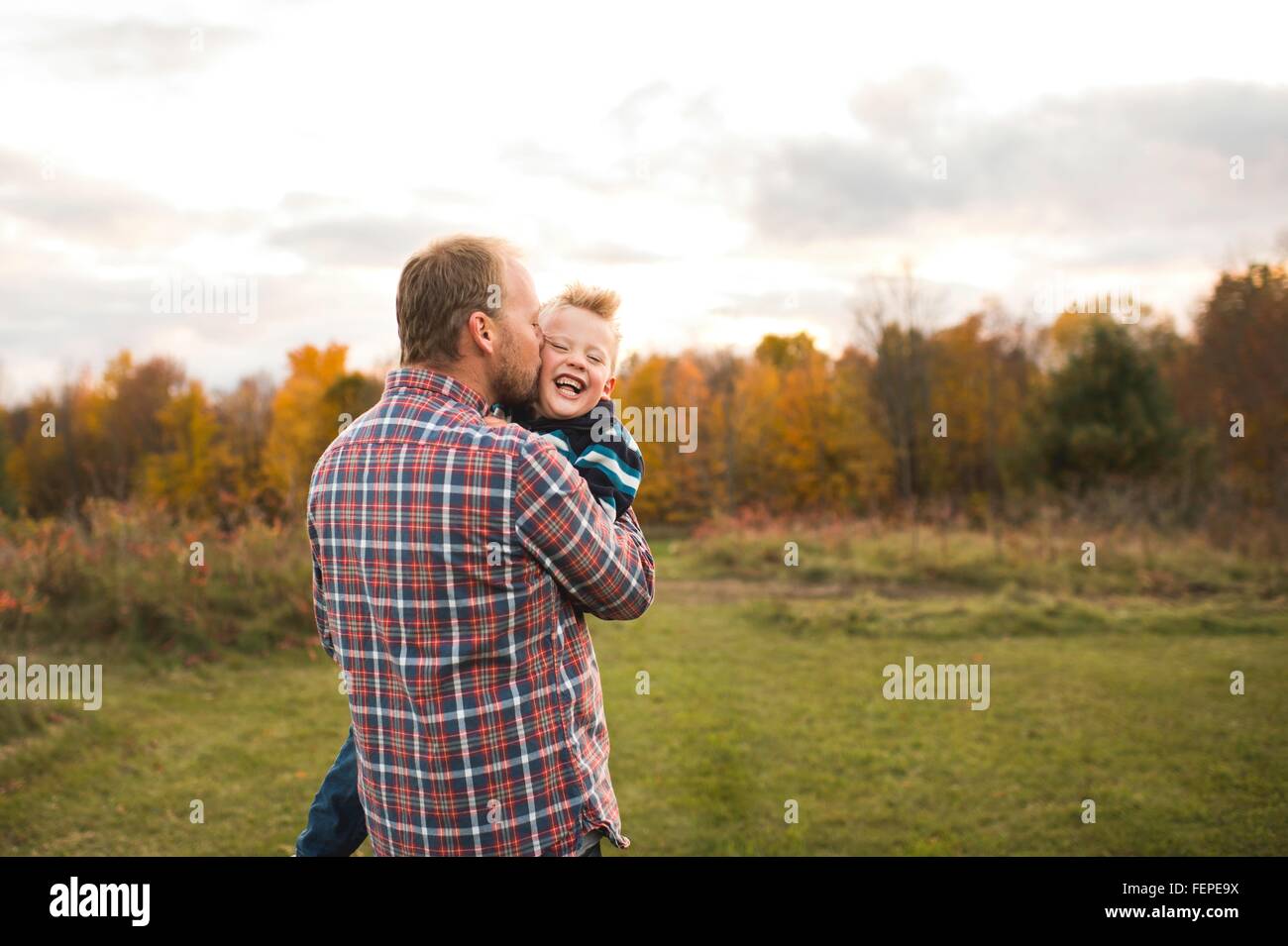Rear view of father carrying smiling son, kissing him on cheek Stock Photo