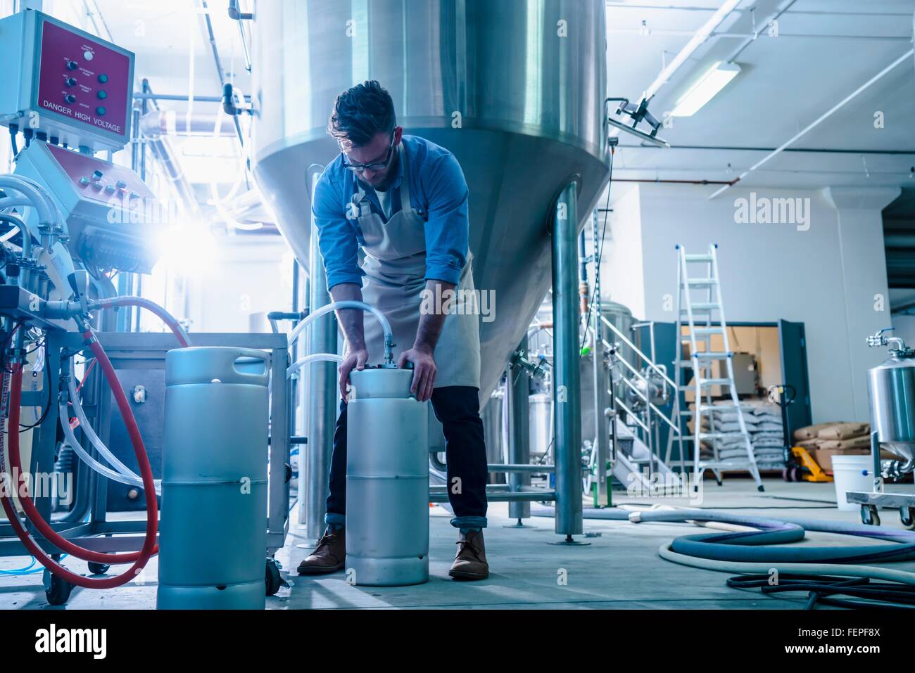 Young man in brewery by conical fermentation tank attaching hose to canisters Stock Photo