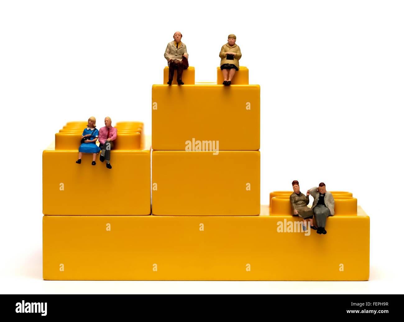 3 miniature figurine couples sitting on interlocking yellow plastic bricks 1st 2nd third pension concept Stock Photo