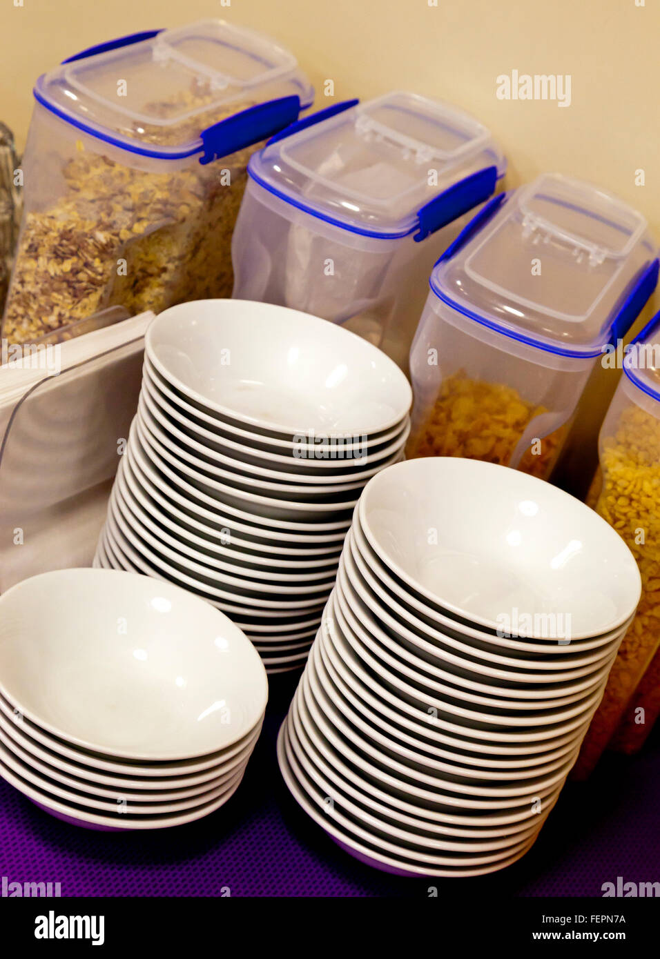 Breakfast cereals in plastic containers and white china bowls stacked up in a communal eating area Stock Photo