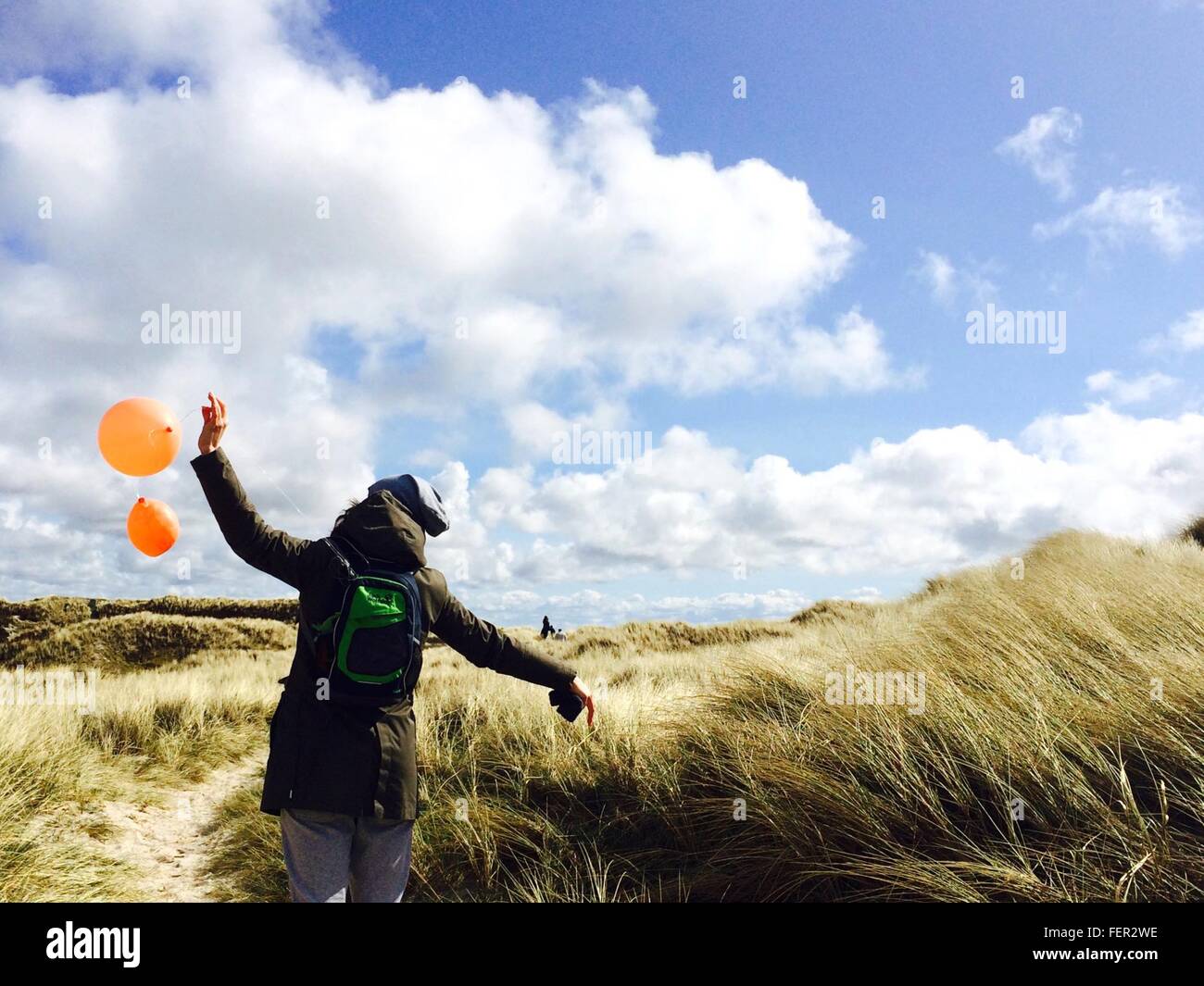 Rear View Of Girl Holding Orange Balloons On Field Against Cloudy Sky Stock Photo