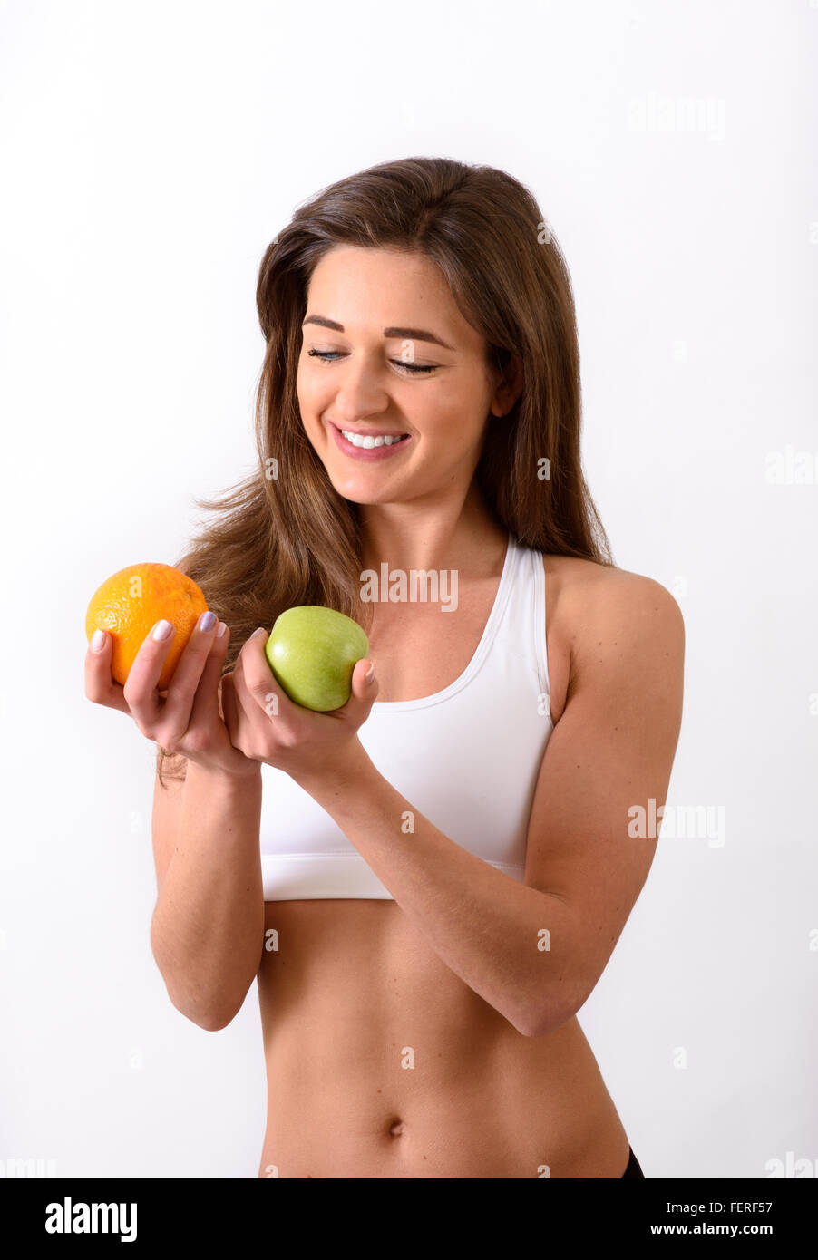 Young slim woman in sports top deciding between an orange and an apple Stock Photo