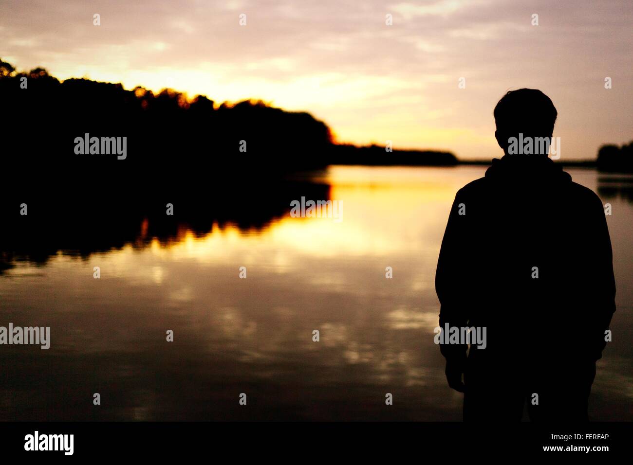 Rear View Of Silhouette Man Standing In Front Of Lake During Sunset Stock Photo