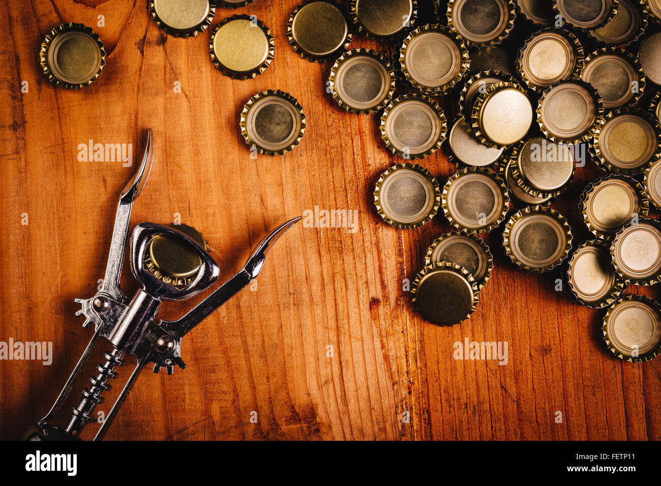Classic bottle opener and pile of beer bottle caps on top of rustic oak wood desk, top view. Stock Photo