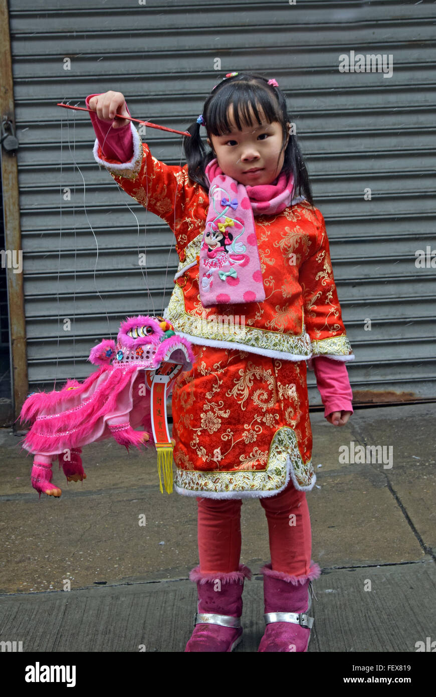 A beautiful 5 year old Chinese girl in a fancy dress & a small dragon at the Lunar New Year parade. Mott St. in Chinatown, NYC Stock Photo